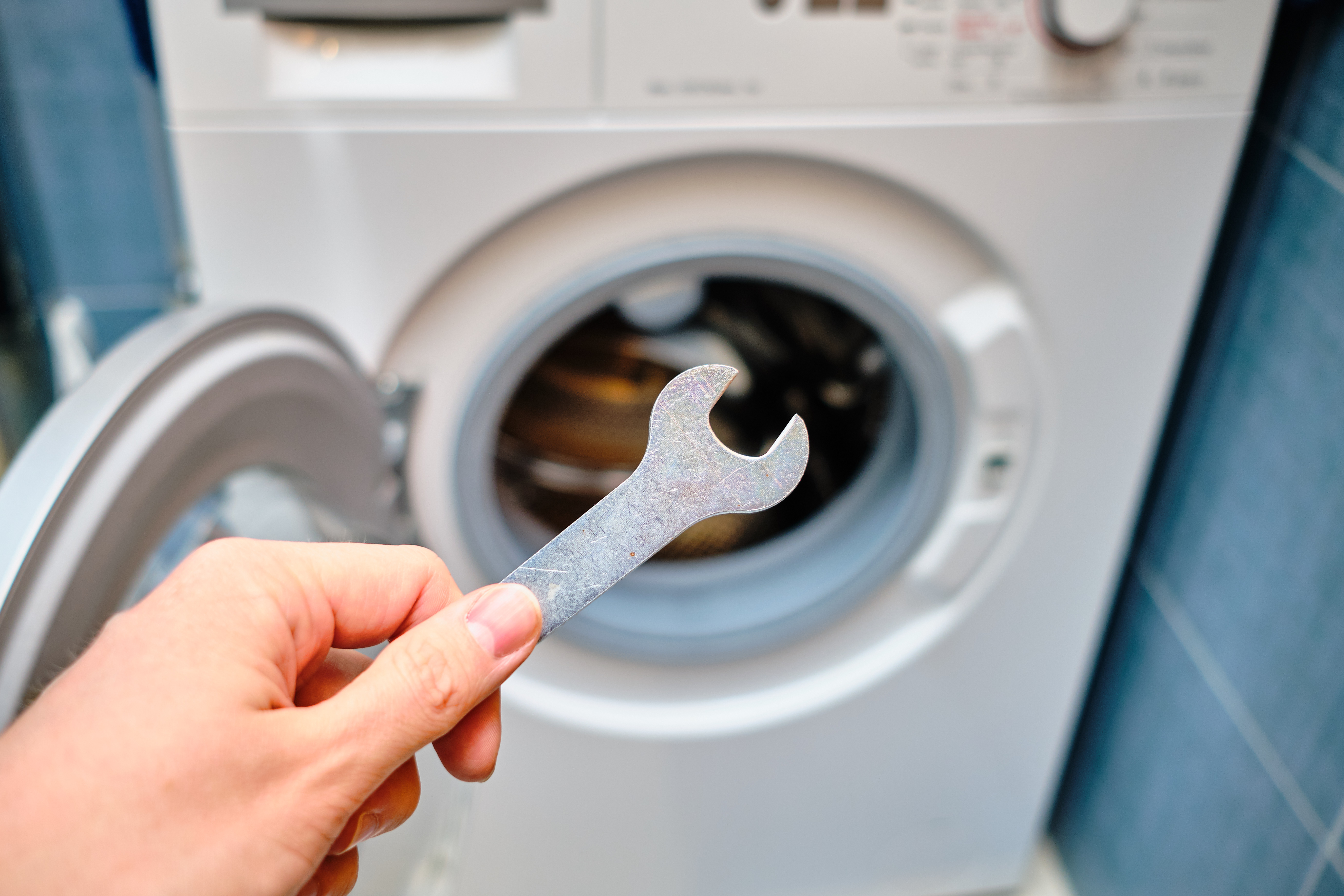 A person holding a wrench with a front load washer in the background 