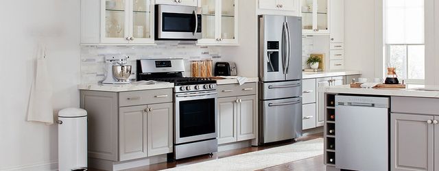 front view of a modern kitchen with white walls, counters, and upper cabinetry with grey lower cabinets and stainless steel appliances including a range, microwave, refrigerator, and dishwasher in an island