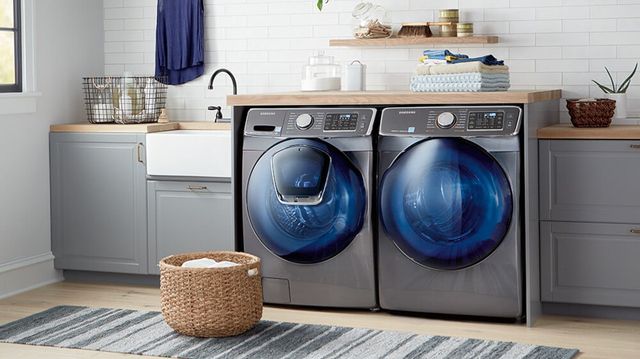 front view of a grey front load washer and dryer in a modern laundry room with white subway tile walls and light wood countertops