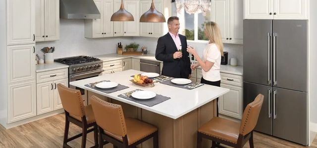 front view of a couple standing in a modern kitchen with stainless steel appliances and white cabinetry