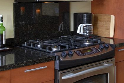 front view of a black gas range in a modern kitchen with black counters and orange walls and cabinetry