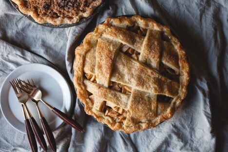 top view of an heirloom apple pie in frame, next to a pecan pie slightly out of frame on a light blue tablecloth