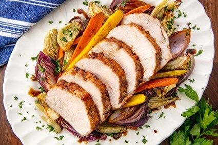 top view of a sliced pork roast and roasted veggies around it on a white plate