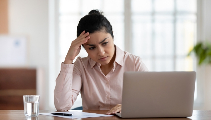 woman with hand on forehead frustrated at computer