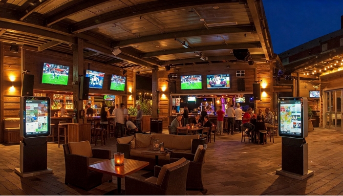 An outdoor dining space with tables, tvs, and many people.