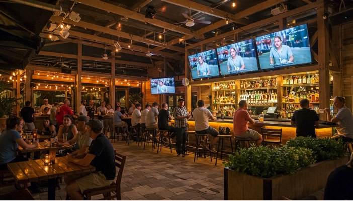 An outdoor bar and entertainment space with mulitple TVs and lots of people.