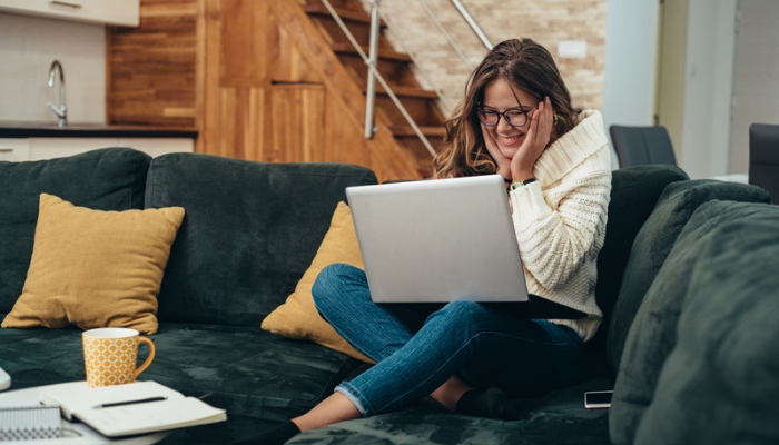 A woman sits on a blue couch using a silver laptop