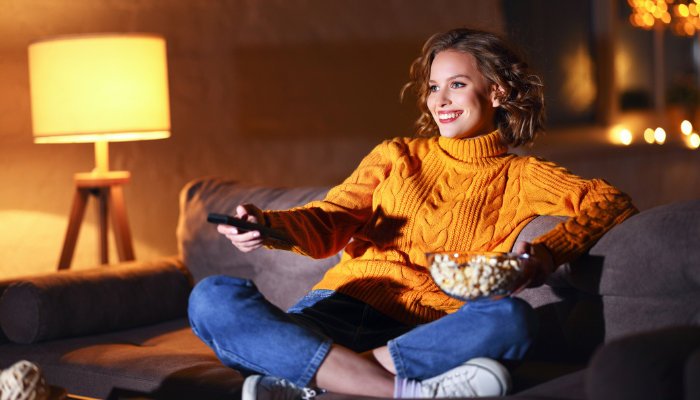 woman watching a movie and eating popcorn at home in a low lit room