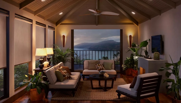 A dimly lit modern sunroom with drawn neutral shades and neutral furniture.