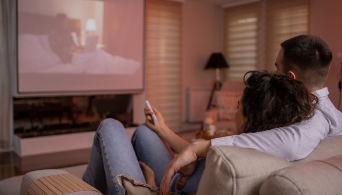 A couple sits together on a couch and watches a movie on their home projector.