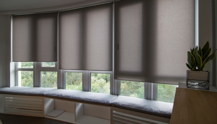 A set of partially closed motorized shades next to a reading bench in a home.
