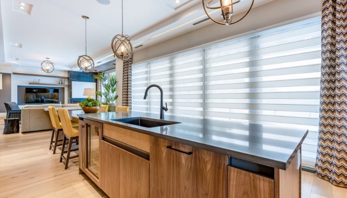 A modern kitchen with white motorized shades and a modern features.
