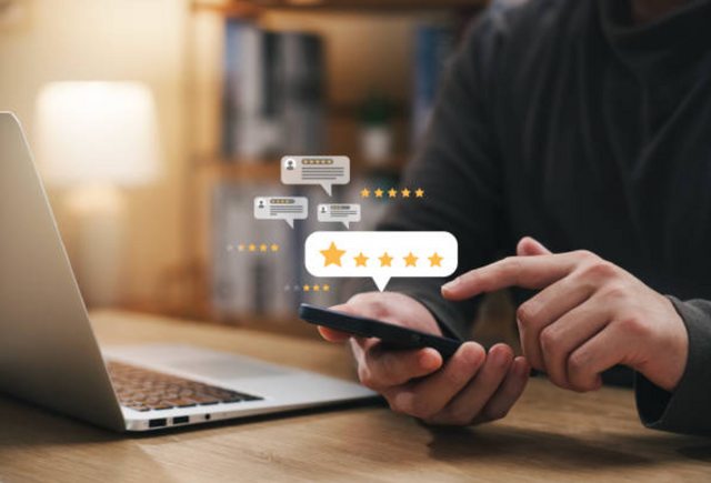 view of a person leaving a review on their phone in front of a laptop, with cartoon stars displaying other happy reviews