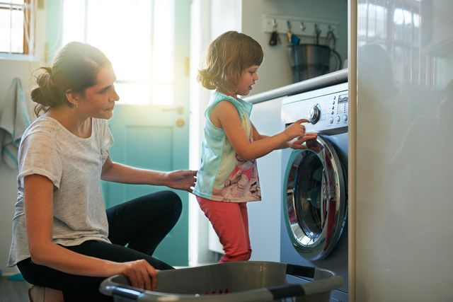 Side view of a mother and daughter doing laundry together in front of a small compact washing machine