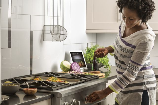 front view of a woman cooking on a rangetop in a white kitchen