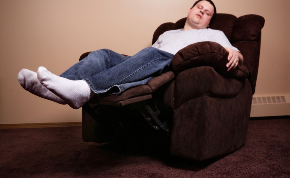 A man sleeps in a brown power recliner