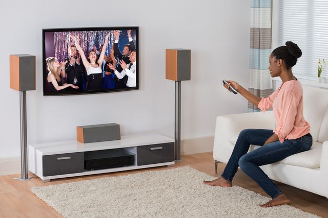 woman clicking on her TV that is surrounded by speakers