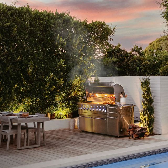 view of an Alfresco grill with smoke flowing out of the opened top, and meats smoking inside in front of a sunset