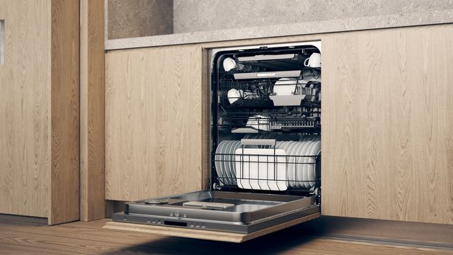front view of an opened Asko dishwasher built into modern light wooden cabinetry and full of dishes