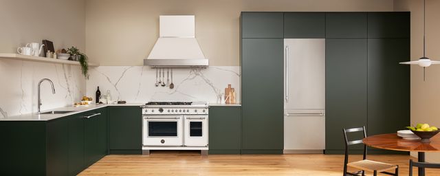 front view of a modern luxury kitchen green cabinets, a white bertazzoni range, and stainless steel refrigerator