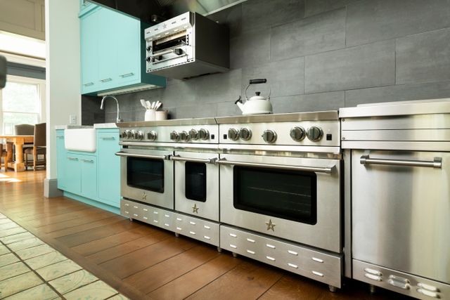 front view of two bluestar ranges in a modern kitchen with light blue cabinetry and a gray backsplash
