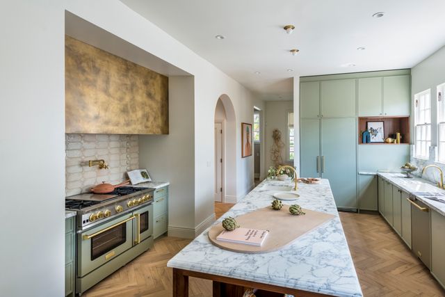 front view of a large modern kitchen with sage green cabinetry, a rage green Bluestar range built into a wall cubby, and pink accents throughout