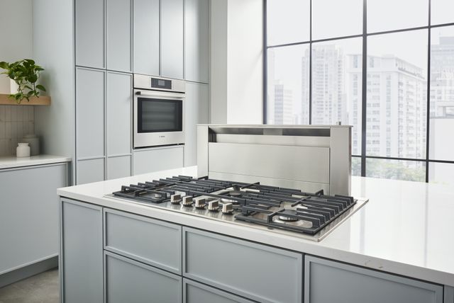 Front view of a modern kitchen with a cooktop and downdraft ventilation hood behind it in the island