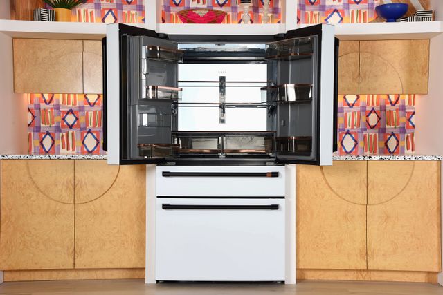 Front view of a modern kitchen with a white cafe french door refrigerator opened to show the inside.