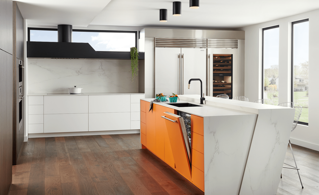 Front view of a luxury, sleek, modern kitchen with a panel ready cove dishwasher slightly opened in an island and a Sub-Zero refrigerator in the background