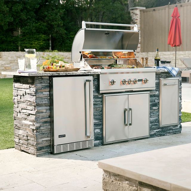 Front view of a Coyote outdoor kitchenette with a grill opened and food displayed