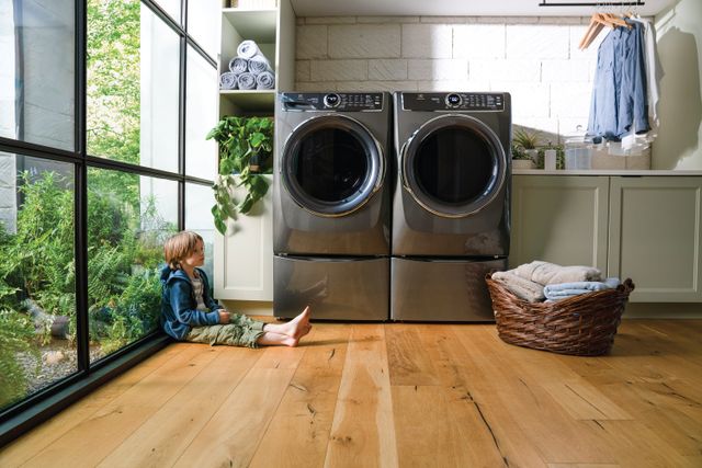 front view of a child sitting in a bright and clean laundry room with an electrolux washer and dryer