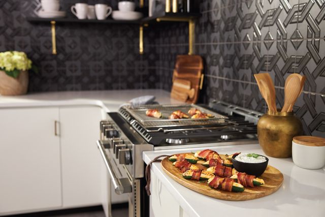side view of a professional range in a white countertop, with jalapeno poppers in the counter and a pan of them on the stove