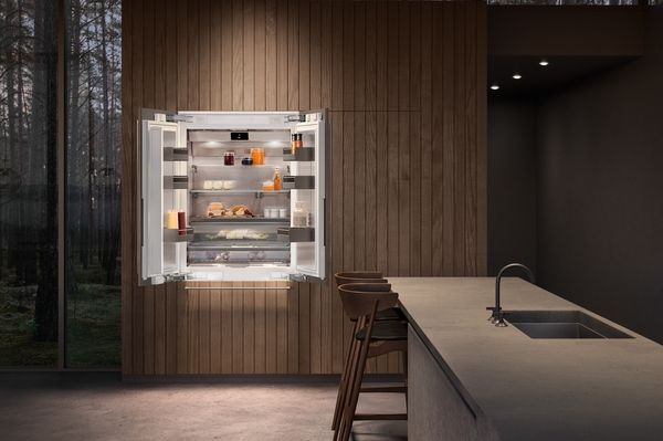 Front view of an opened Gaggenau refrigerator in a contemporary kitchen with wood panel cabinetry and an island.