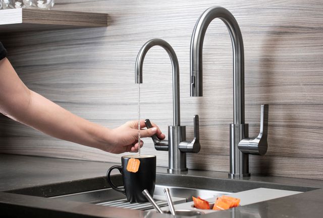 Close view of a mug of tea being filled with an instant hot water faucet over a galley sink