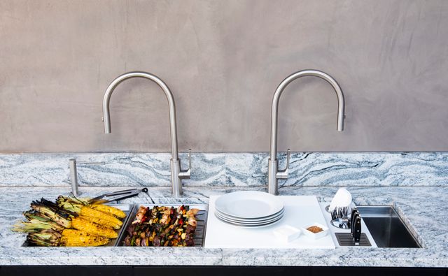 front view of a workstation sink in a marble countertop being used to serve corn and kebabs outside