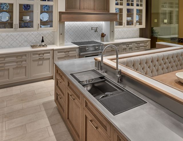 front view of a modern luxury kitchen with a workstation sink installed in the countertops in the foreground, and a range in the countertops in thebackground