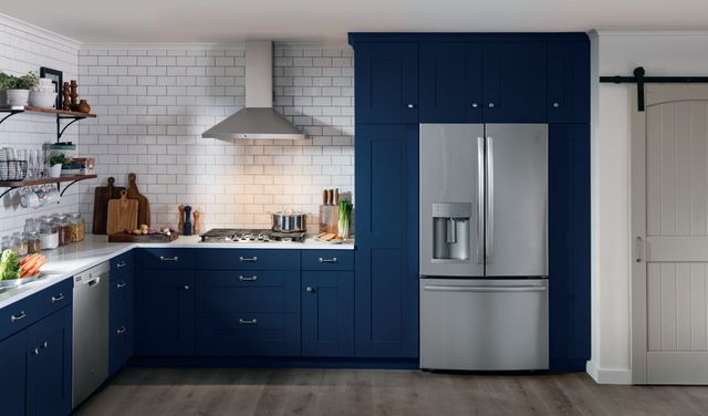 front view of a modern kitchen with blue cabinets and white backsplash with a stainless steel french door refrigerator and dishwasher