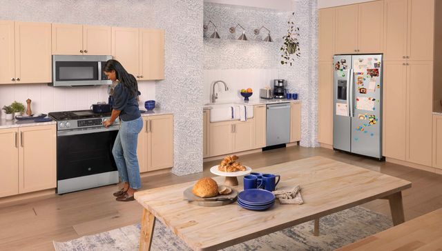 View of a modern kitchen with stainless steel appliances and a woman preheating the oven.