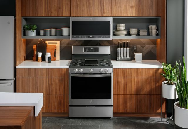 front view of a ge range with an over the range microwave in a modern kitchen with brown wooden cabinets and white countertops