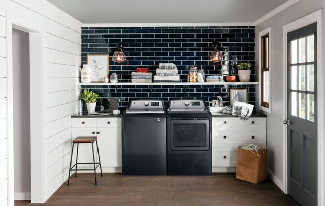 front view of a modern laundry room with white cabinets, blue tile walls, and a grey washer and dryer