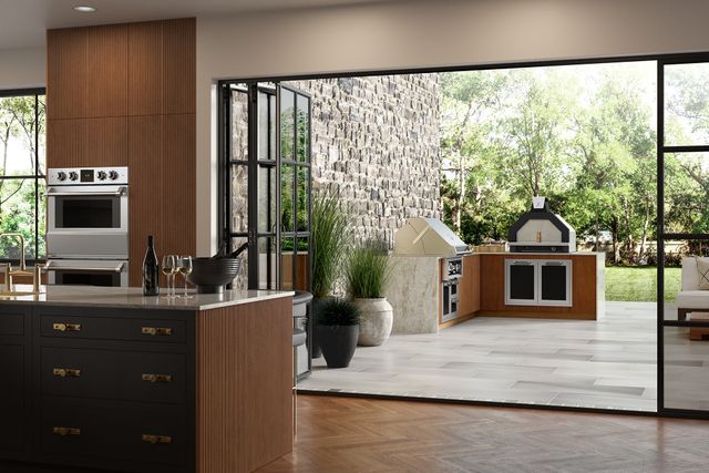 front view of a luxury modern kitchen with doors opening to an outdoor patio with a pizza oven