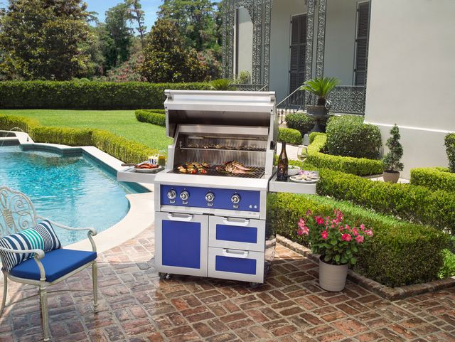 front view of a Hestan freestanding grill with meats cooking on it poolside