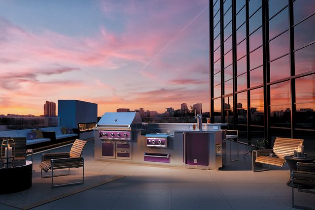 front view of a rooftop kitchen with high end hestan grill and outdoor kitchen appliances in front of a pink and blue sky