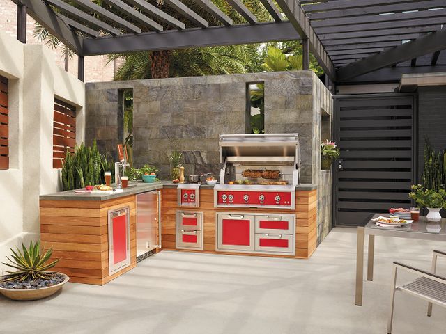 front view of a red hestan built in grill in a modern outdoor kitchen with other red and stainless steel hestan appliances