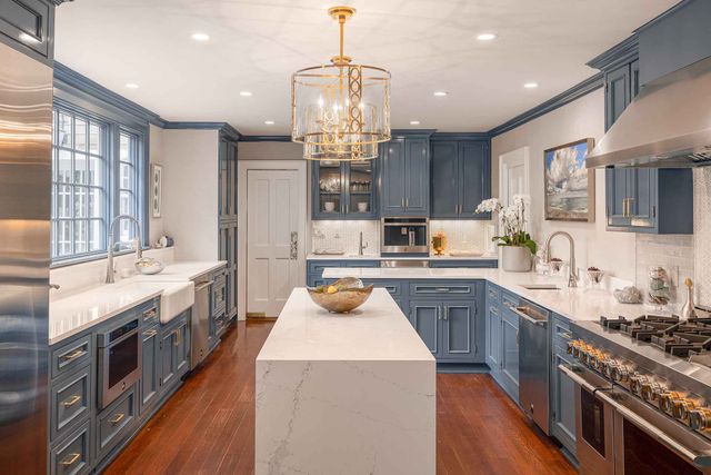 Front view of a modern kitchen with white countertops, blue cabinetry, and stainless steel JennAir appliances.