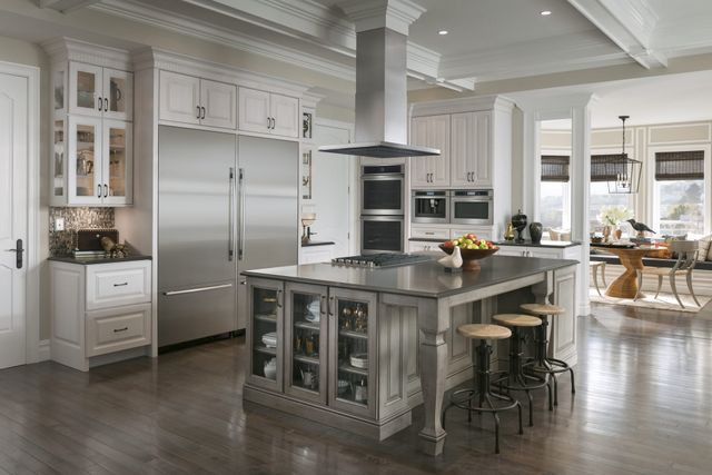 Front view of a large luxury kitchen with white walls and cabinetry, and various stainless steel JennAir appliances.