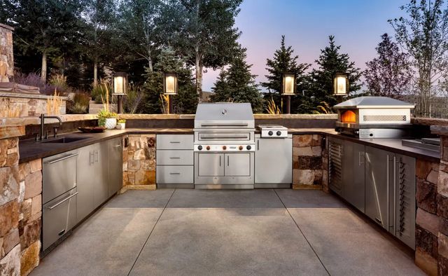 front view of a modern outdoor cooking station with a grill, side burner, pizza oven, outdoor storage, a sink, and more