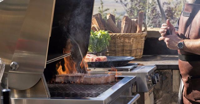 Side view of a man grilling two large steaks on a Kalamazoo grill