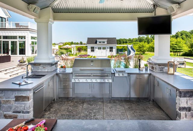 Front view of a modern outdoor kitchen with stainless steel appliances and an outdoor sink and fridge