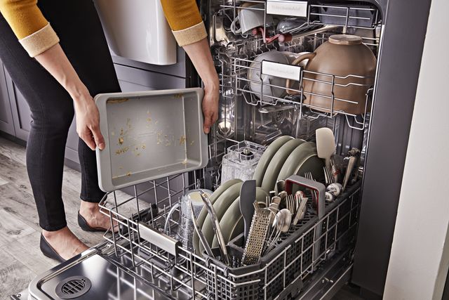 Credit: KitchenAid Front view of a modern kitchen with a woman loading her KitchenAid dishwasher
